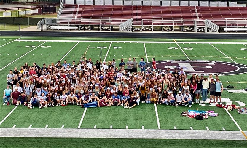 A large group of students takes a photo on the football field